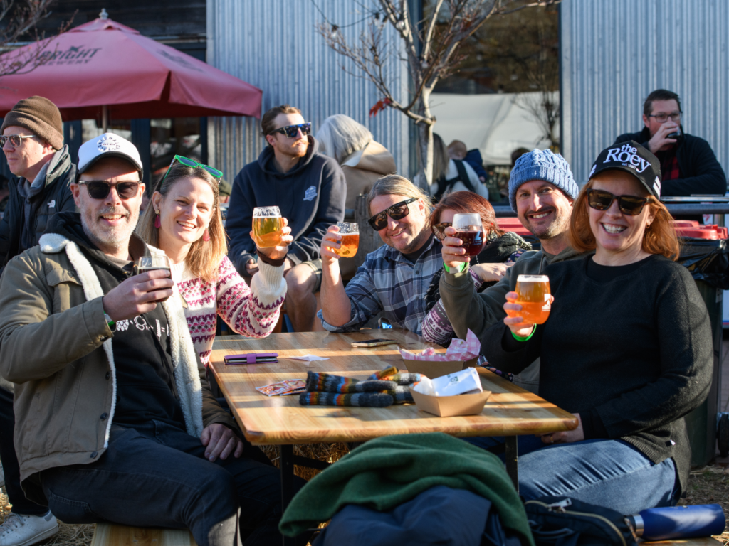Darker Days guests enjoying a beer in the winter sun with smiles on their faces, cheers with beers.