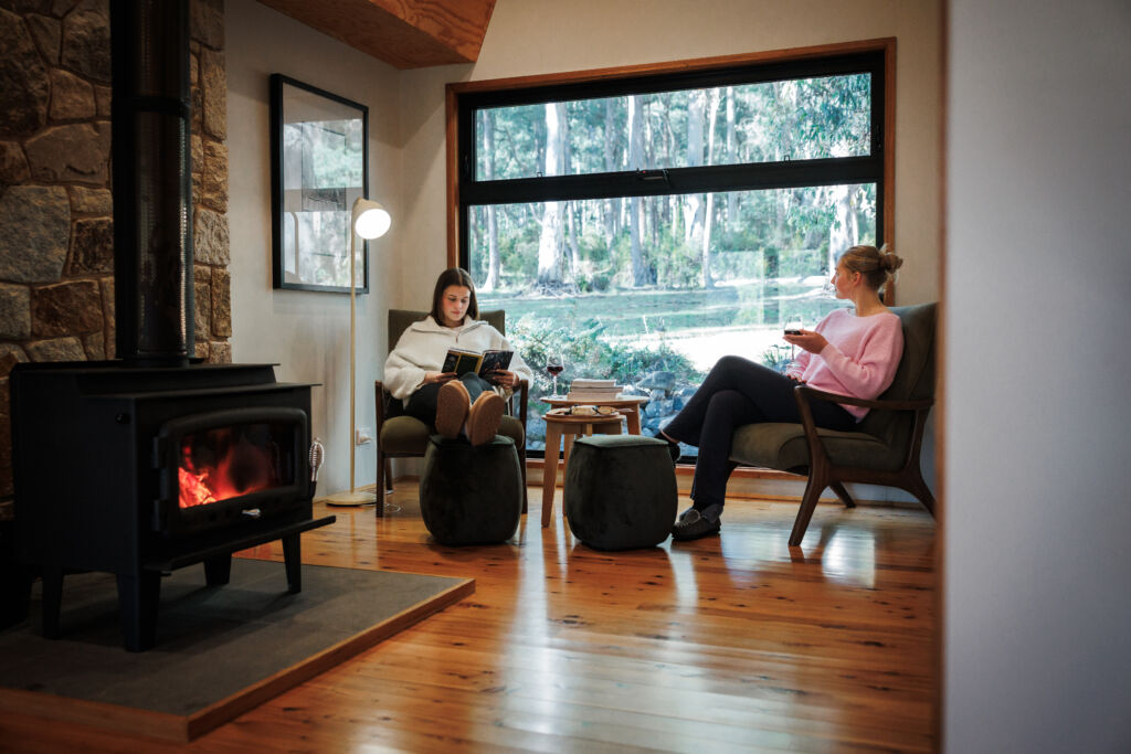 Two women sitting in front of the fire reading a book and drinking red wine, relaxing